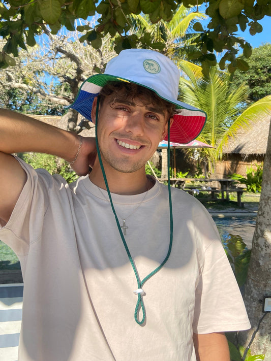 A person wearing a white and red South African patch hat with an adjustable drawstring, standing outdoors.