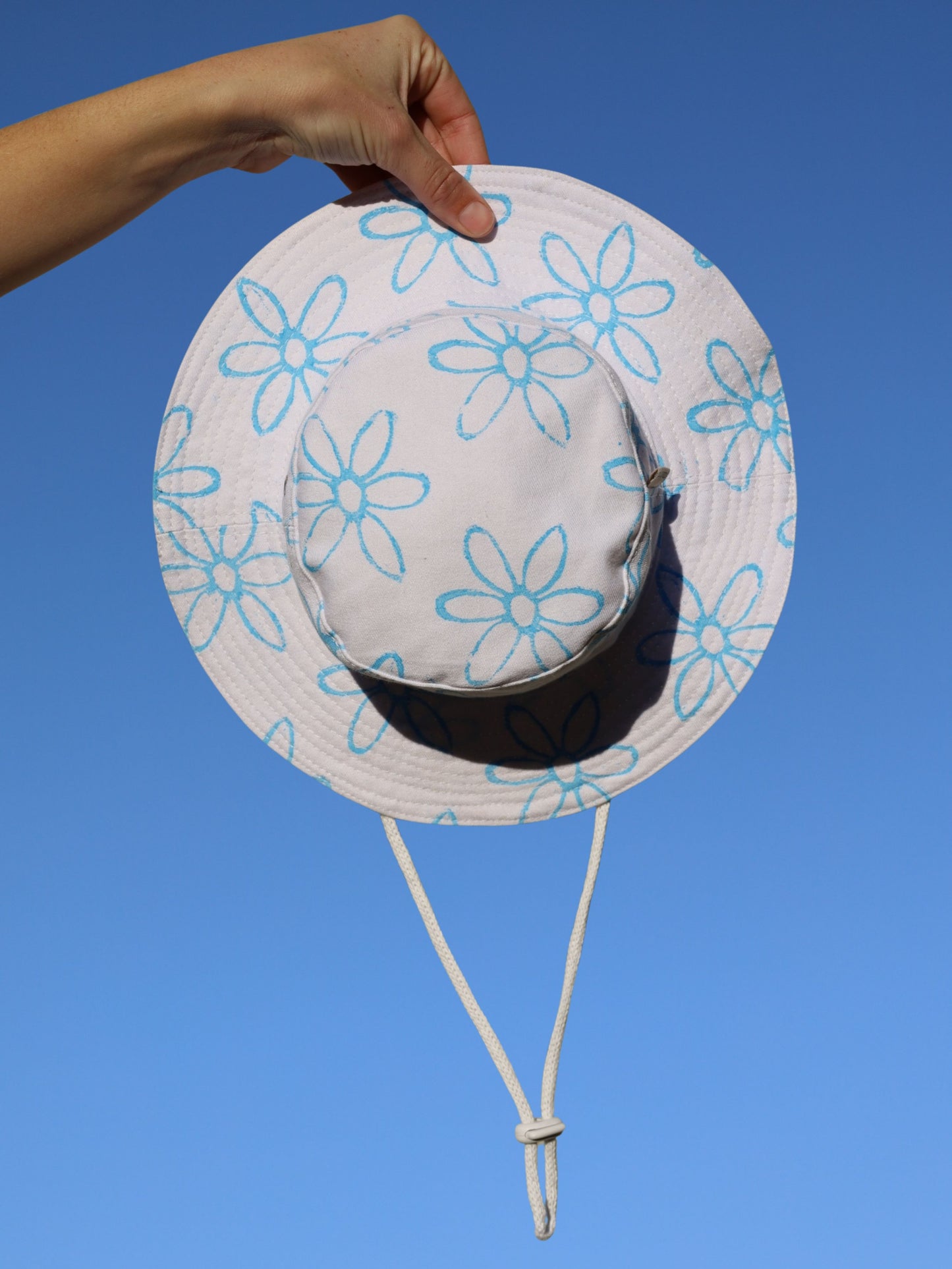 White sun hat with blue floral patterns held against a clear blue sky