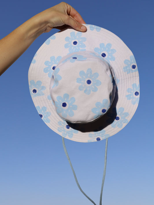 White sun hat with blue floral patterns held against a clear blue sky