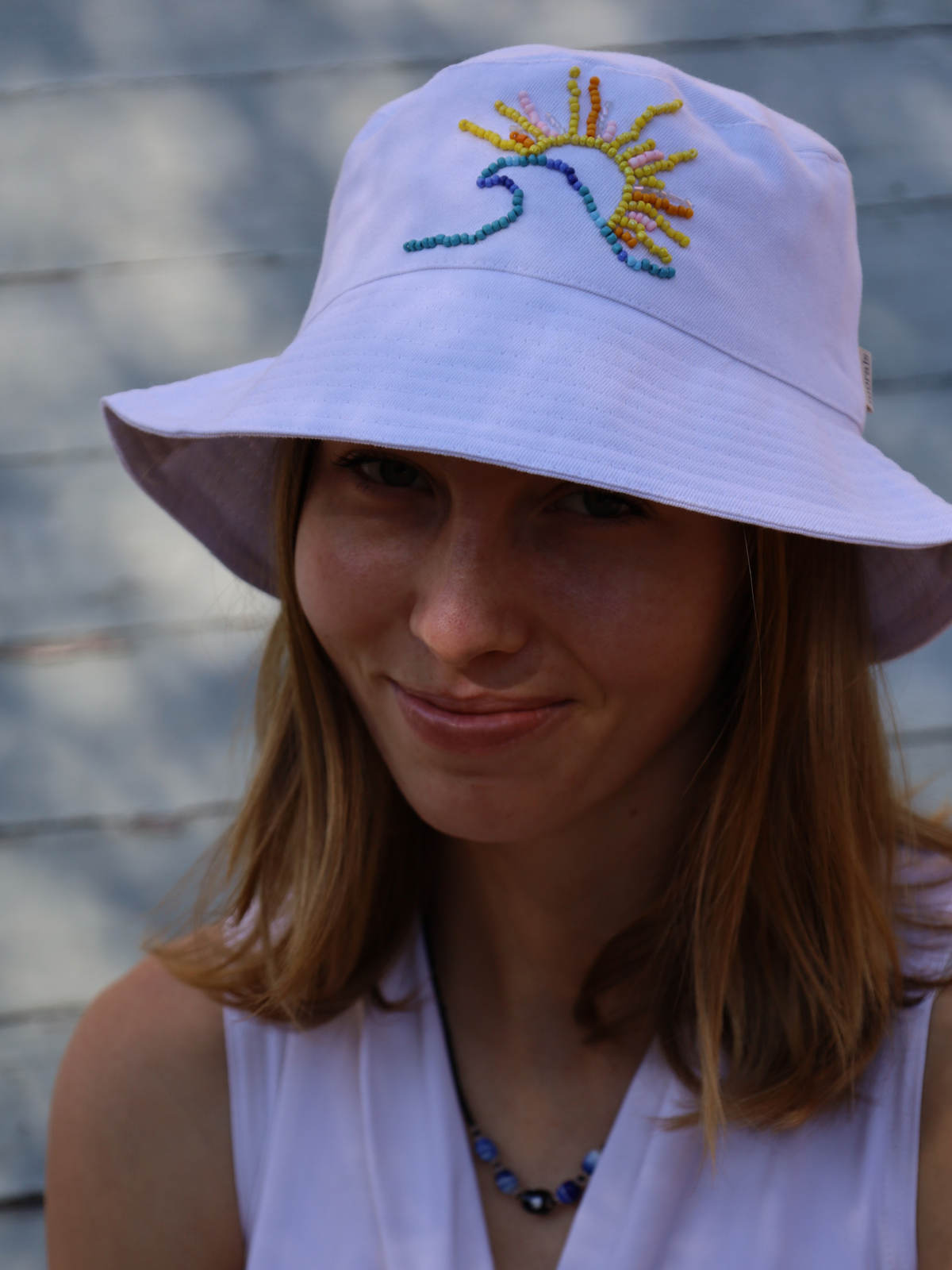 Person wearing a white bucket hat with a colorful sun design in beads. Beaded and made in South Africa