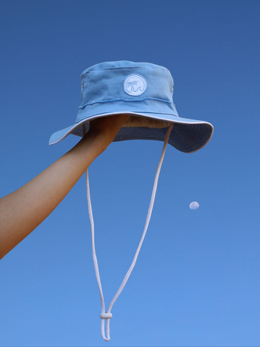 Blue bucket hat held against a clear blue sky with a moon visible.