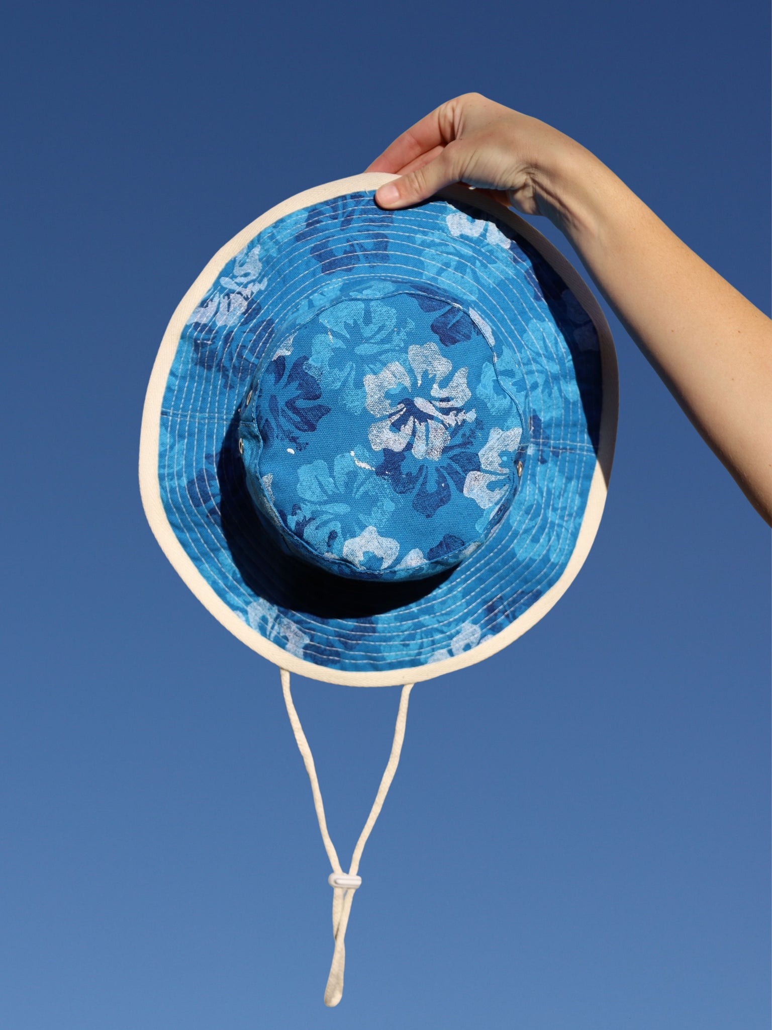 Blue floral-patterned sun hat held against a clear blue sky