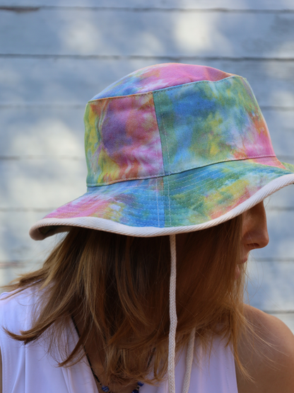 Person wearing a colorful tie-dye bucket hat against a wooden fence background